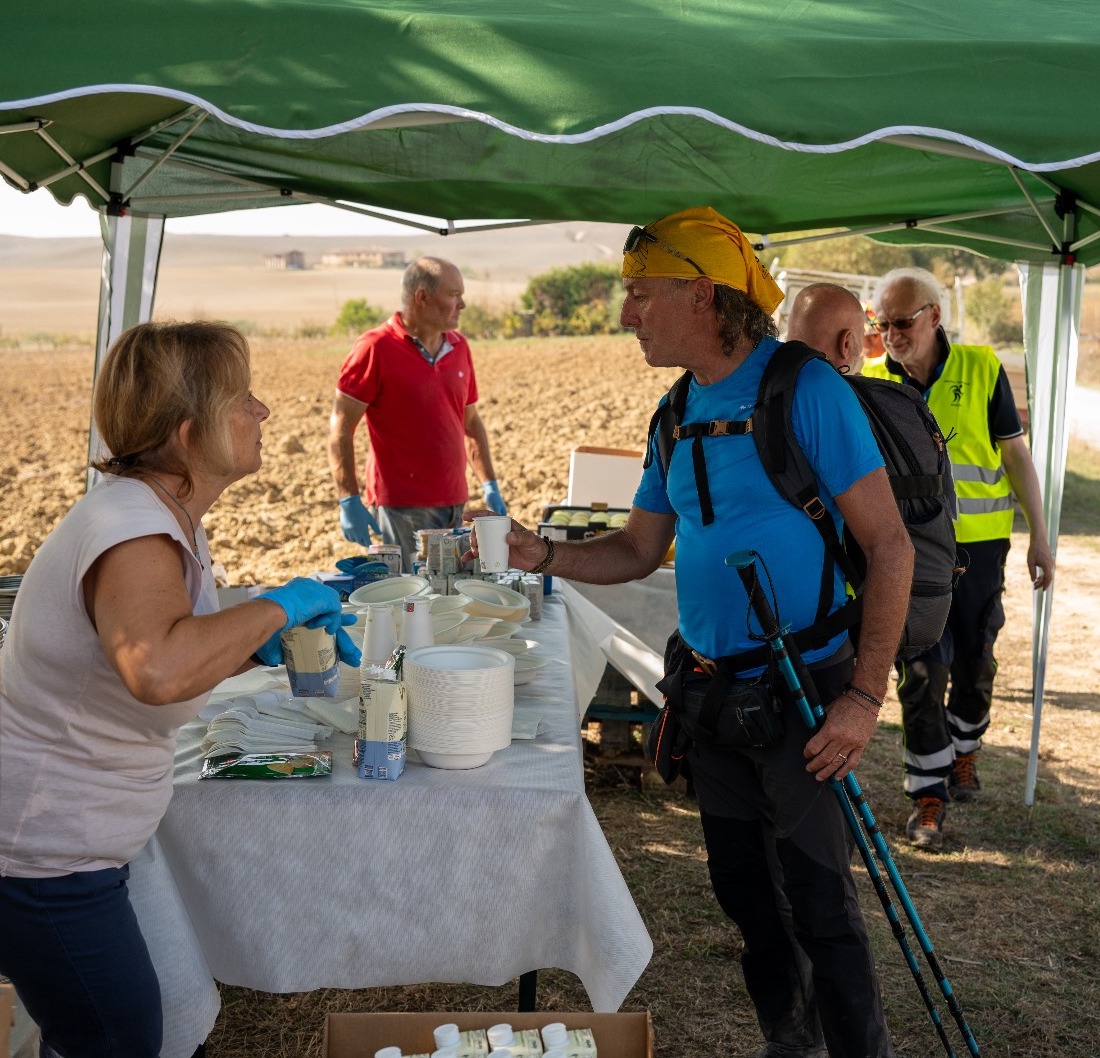 Persona che serve cibo a camminatori, volontari sullo sfondo.